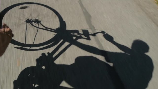 Pedaling rider and his shadow on the road.