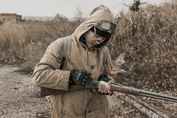 Fototapeta premium wandering boy. boy with a gun. boy goes to an abandoned building. boy stands in front of a building. Post apocalypse. Boy traveling on foot in a post-apocalyptic world in search of food. 