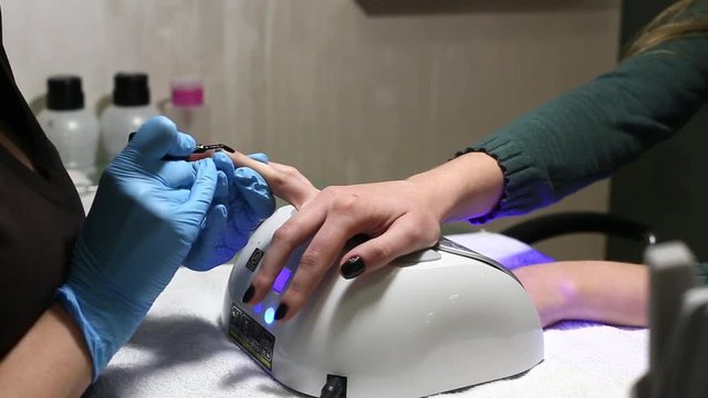 manicurist makes the manicure for young caucasian woman in beauty salon. hands close up