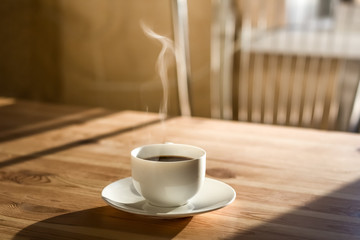 Cup of morning coffee. Kitchen interior in natural light, wood table with hot steaming drink on it