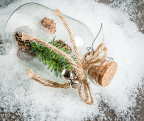 Christmas decorations on a wooden table: a glass jar with a sprig of fir tree and cones inside an hill of artificial snow, copy space 