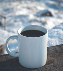cup of hot coffee in the winter on a snow-covered wooden table in nature