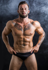 Fototapeta na wymiar Handsome shirtless muscular man in briefs, standing, on dark smoky background