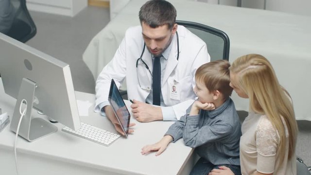 Male Doctor Consults Young Boy and His Mother with a Help of a Tablet. They Smile and talk Warmly.  Shot on RED Cinema Camera in 4K (UHD).