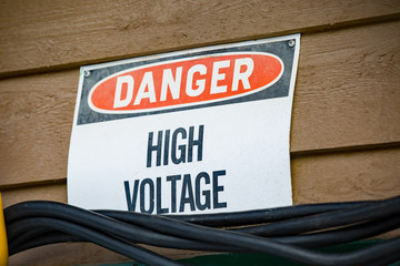 sign with the words danger high voltage on it with cables suspended underneath with wooden siding