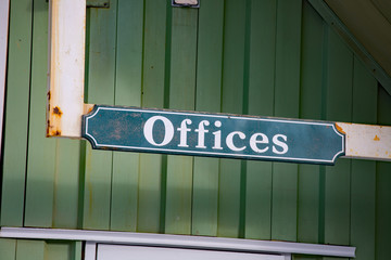 sign with the word offices white on blue background hung in front of green metal siding