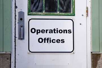 sign with the words operation offices on white background mounted on a well used door with green window frame