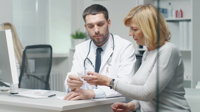 Doctor Writes Prescription to his Mid Adult Female Patient. They Talk and Smile. Shot on RED Cinema Camera in 4K (UHD).