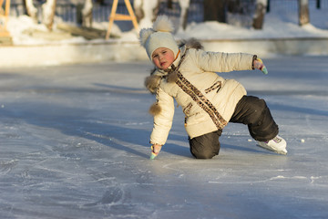 A child on a cold day in a warm jacket and hat fell to the ice skating.