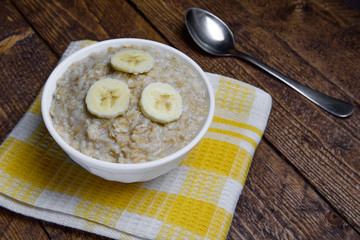 oatmeal in a beautiful white bowl on a warm wooden background with slices of bananas