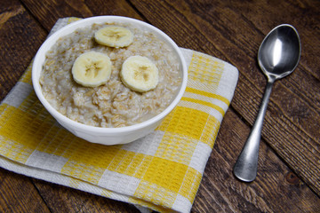 oatmeal in a beautiful white bowl on a warm wooden background with slices of bananas