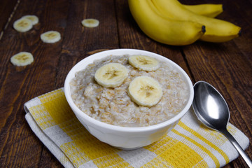 oatmeal in a beautiful white bowl on a warm wooden background with slices of bananas