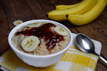  oatmeal in a beautiful white bowl on a warm wooden background with slices of bananas  and jam 