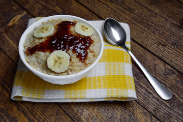  oatmeal in a beautiful white bowl on a warm wooden background with slices of bananas  and jam 