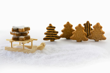 Fototapeta na wymiar Wooden sled carries cinnamon star cookies through the snowy forest with christmas trees from gingerbread