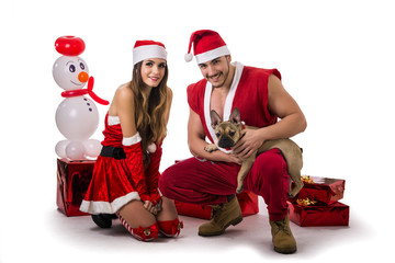 Handsome young man and pretty young woman in Santa Claus hat and costume, with pug dog, standing holding colorful festive Christmas gifts to celebrate the season, on white background