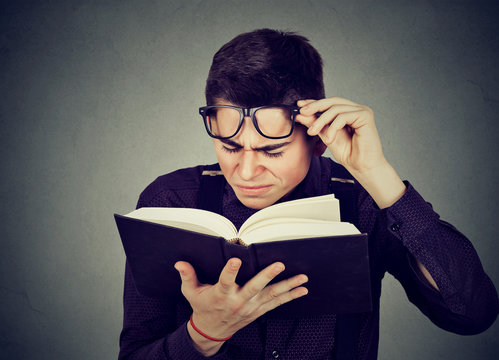 man with eye glasses trying to read book has sight problems
