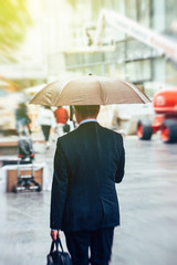 Businessman under rain walking toward sun