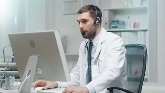 Male Doctor Consults Patients on the Internet. He Sits before His Personal Computer and Wears Microphone.  Shot on RED Cinema Camera in 4K (UHD).
