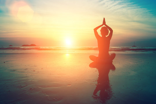 Woman practicing meditation near the ocean. Yoga silhouette...