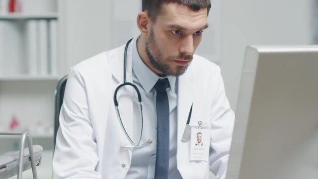 Close-up of a Male Doctor is Working at His Desk. He Uses Personal Computer and Consults Documents. Shot on RED Cinema Camera in 4K (UHD).