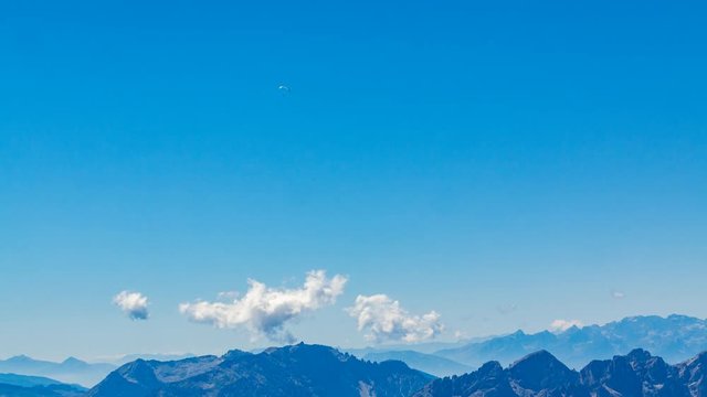 Timelapse of paragliders flying high above alpine peaks on sunny summer day