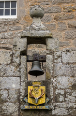 Cowdor, Scotland - June 2, 2012: The black bell hangs in gray stone niche. Golden coat of arms and slogan, Be Mindful. In the arch above the entrance gate of historic Cowdor Castle. 