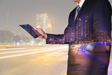 Double exposure of businessman looking the tablet, urban, city and street at night as Business, Technology and Communication concept.