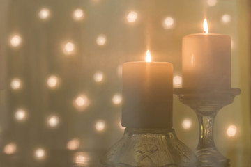 horizontal image of a soft look to two thick Christmas candles burning with blurred lights in the background.