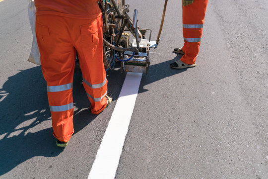 Thermoplastic spray marking machine during road construction.
Worker painting white line on the street surface (Road worker painting)

