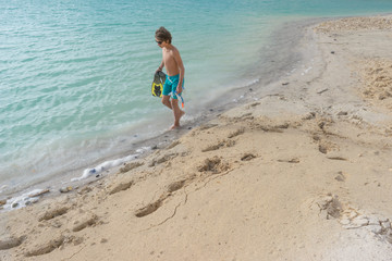 boy standing on the beach. boy looks into the distance. a boy in sunglasses. boy in swimming shorts. boy naked. boy on the white sand. boy near the azure sea. boy with flippers and mask for diving