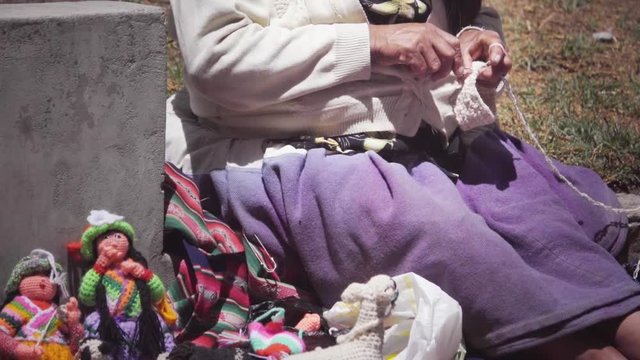 Indigenous Woman crocheting traditional dolls on the streets of Peru.