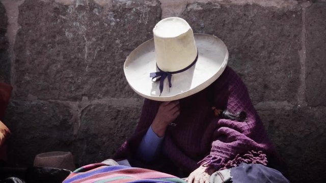 Indigenous woman seated on the street wearing a traditional palm hat