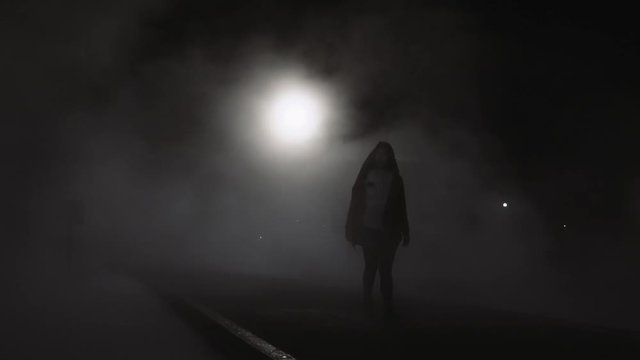 Silhouette of woman walking through the mist  at night. Illuminated by night. 4k