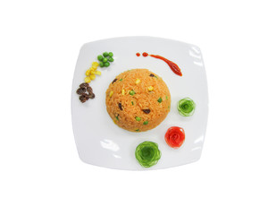 Orange fried rice decorate with vegetable such as currant, corn, peas, Japanese cucumber carving and tomato carving. The white dish on sand.