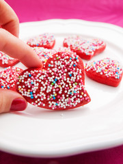 Homemade heart-shaped red cookies decorated with colorful sprink