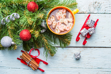 Cup of cocoa with marshmallows and christmas tree with toys on white wooden background.