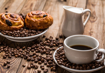 Coffee cup with milk jug and cinnabons on wooden background.