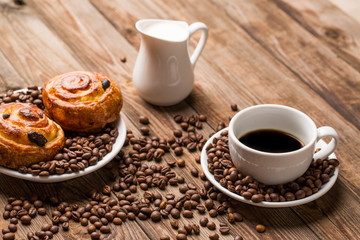 Coffee cup with milk jug and cinnabons on wooden background.