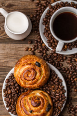 Coffee cup with milk jug and cinnabons on wooden background.