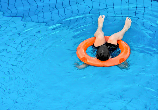 Little boy floating with an orange ring at the swimming pool