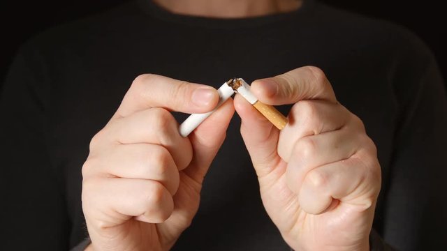 Young adult man holds a cigarette at hands and break it