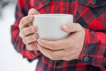Close up of a man holding a cup of tea from white cup outdoors