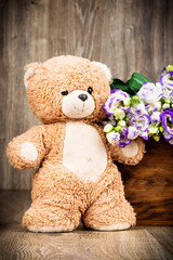 Bunch of flowers and a teddy bear on wooden background