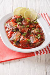 Stewed sardines in tomato sauce with lemon and parsley close-up on the table. vertical