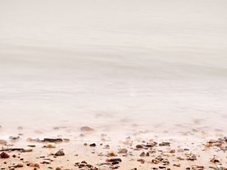 Pebbles on sandy beach against foamy sea water. Natural romantic offshore