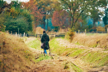 Woman with shoulder bag walking in field with autumn trees.