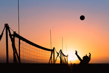 Silhouette of male volleyball player at sunset jumping to spike