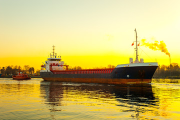 Obraz premium Tugboat assisting cargo ship in port at sunrsie.