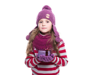 Cute smiling little girl wearing purple knitted scarf, hat and gloves, holding christmas gift isolated on white background. Winter clothes and christmas concept.